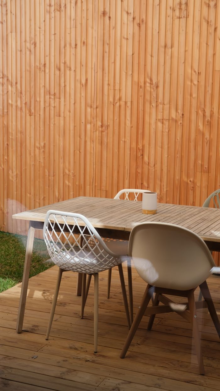 Stylish outdoor patio featuring a wooden table and chairs against a wooden fence.